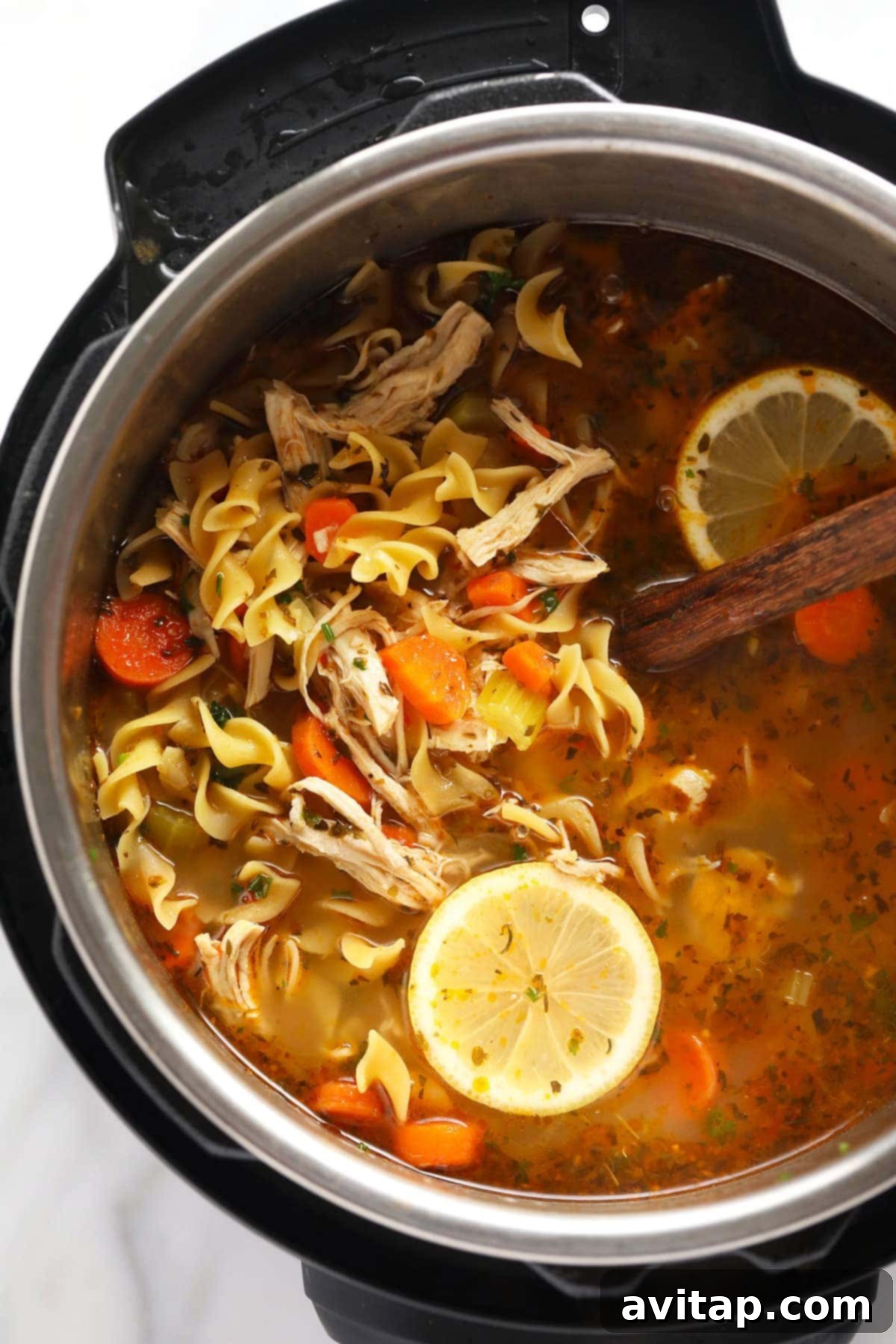 Instant Pot chicken noodle soup in the Instant Pot with a lemon wedge and ladle, ready to be served.