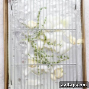 A baking sheet lined with foil, showing a bed of onions, garlic, thyme, and liquid, ready for the wire rack and chicken.