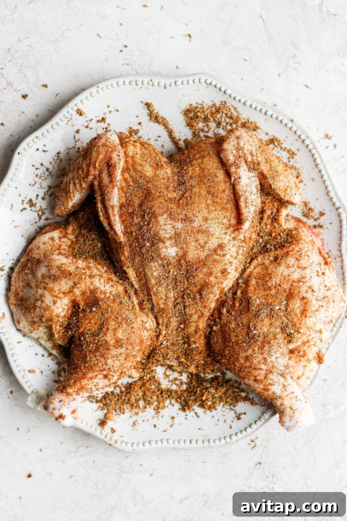 Close-up of raw spatchcock chicken generously coated with a savory dry rub seasoning blend, ready for roasting.