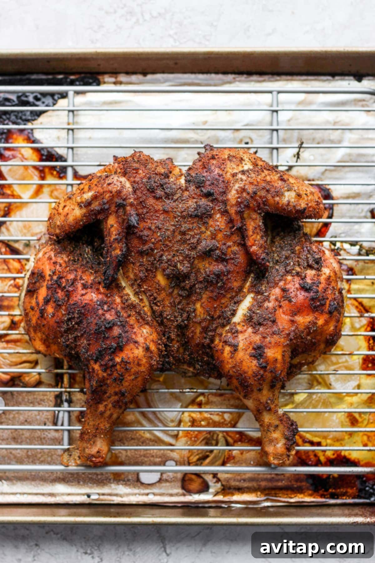 A whole spatchcock chicken resting on a baking sheet after being perfectly roasted, showing the rich golden-brown skin.