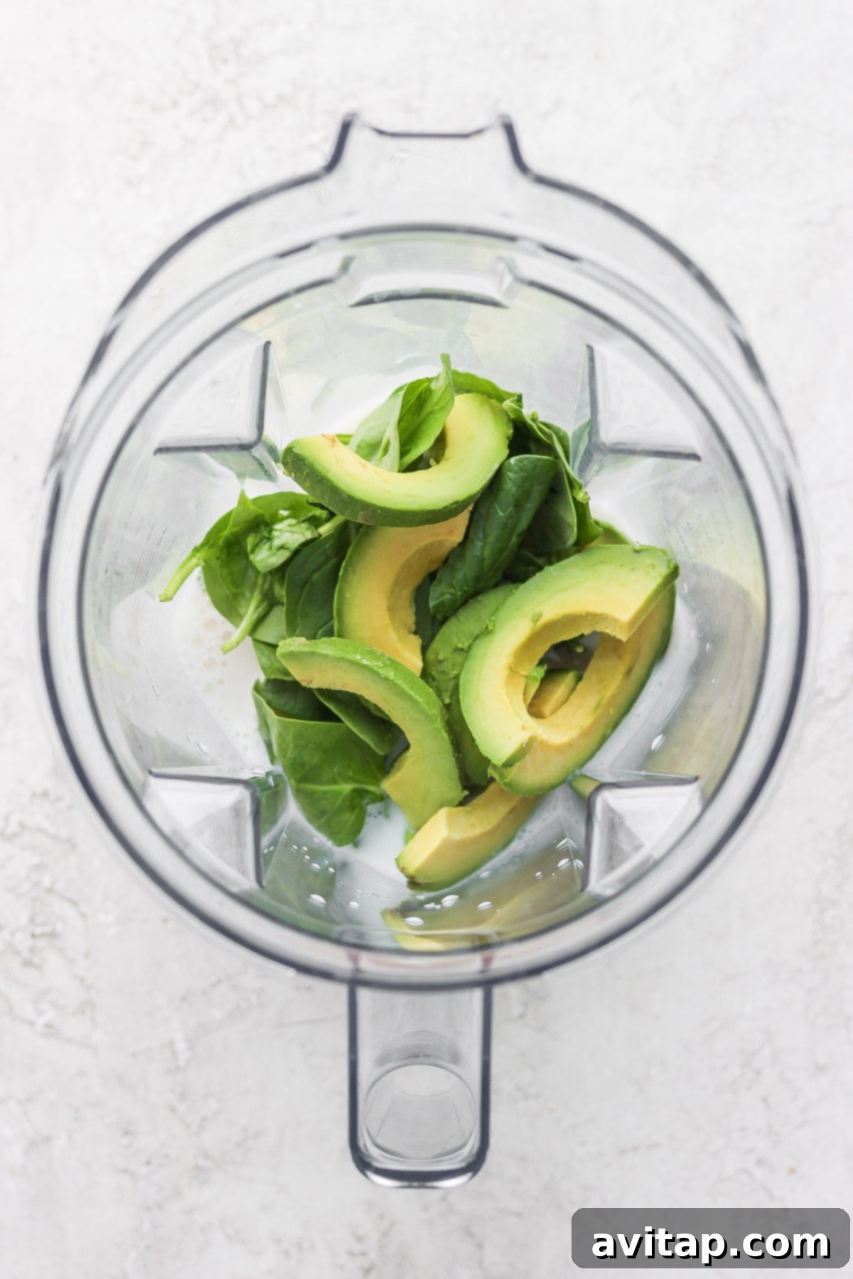 Ready to Blend: Avocado Smoothie All four avocado smoothie ingredients – frozen avocado, spinach, banana, and almond milk – placed inside a blender, ready for blending.