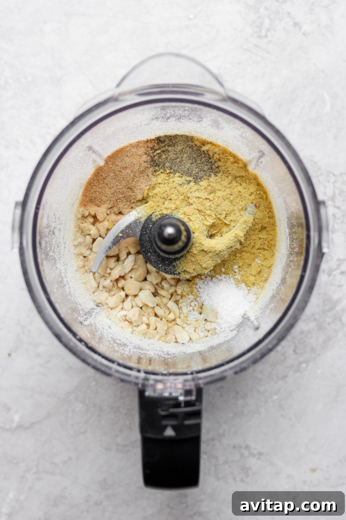 Raw cashews being pulsed in a food processor, starting the vegan parmesan cheese creation process.