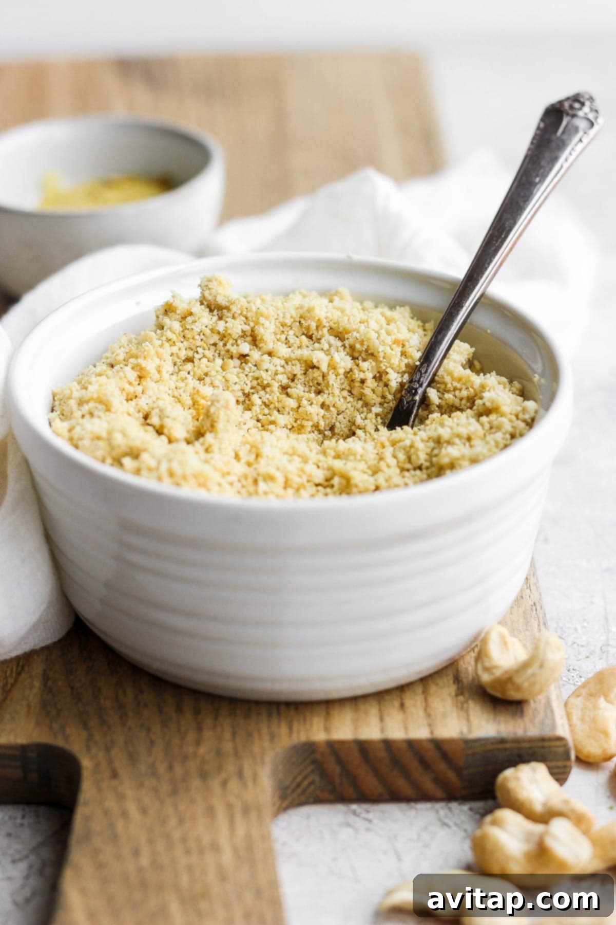 A bowl of vegan parmesan cheese with a small wooden spoon, ready to be served or stored.