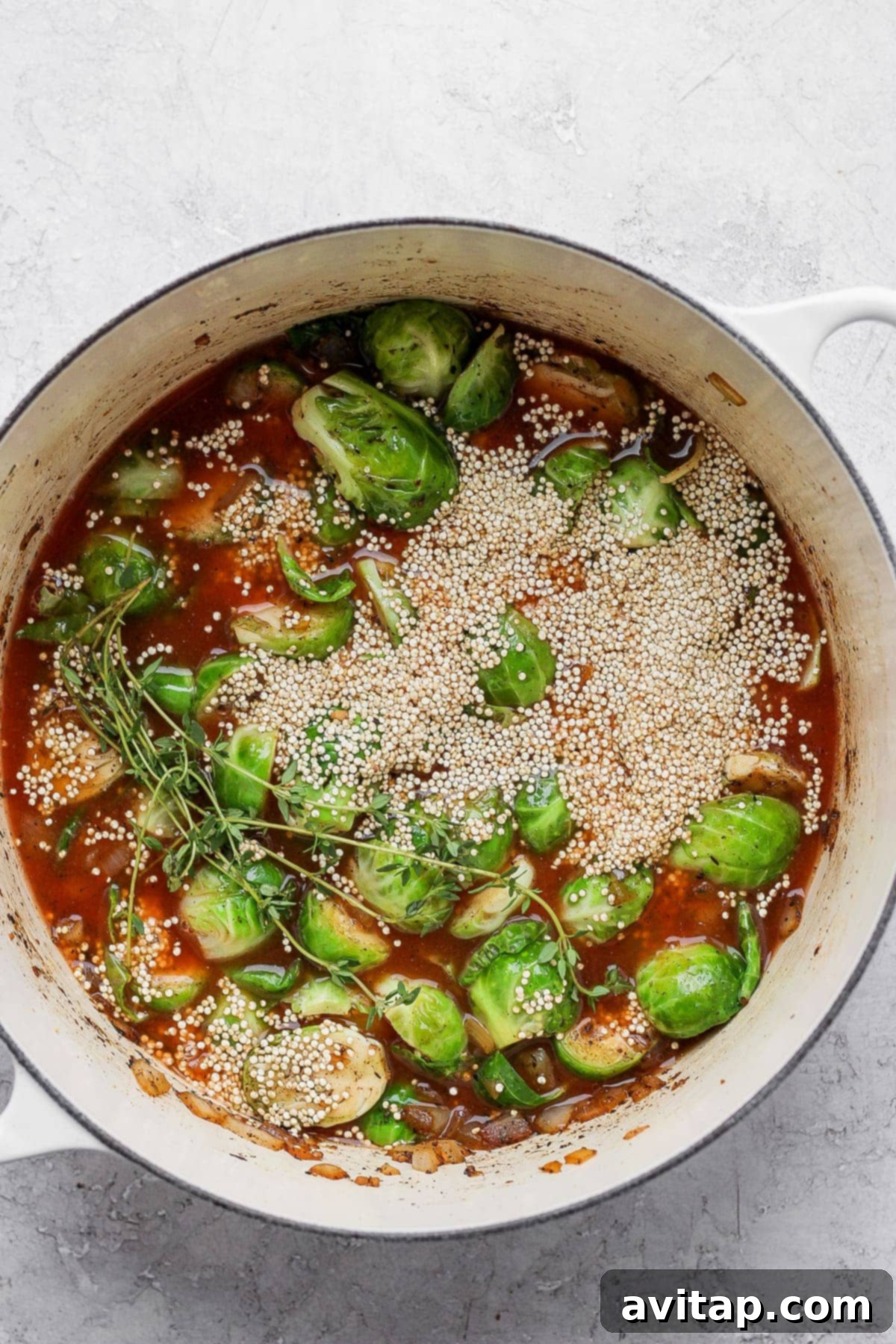 Uncooked quinoa, chicken broth, and fresh Brussels sprouts combined in a Dutch oven before baking.
