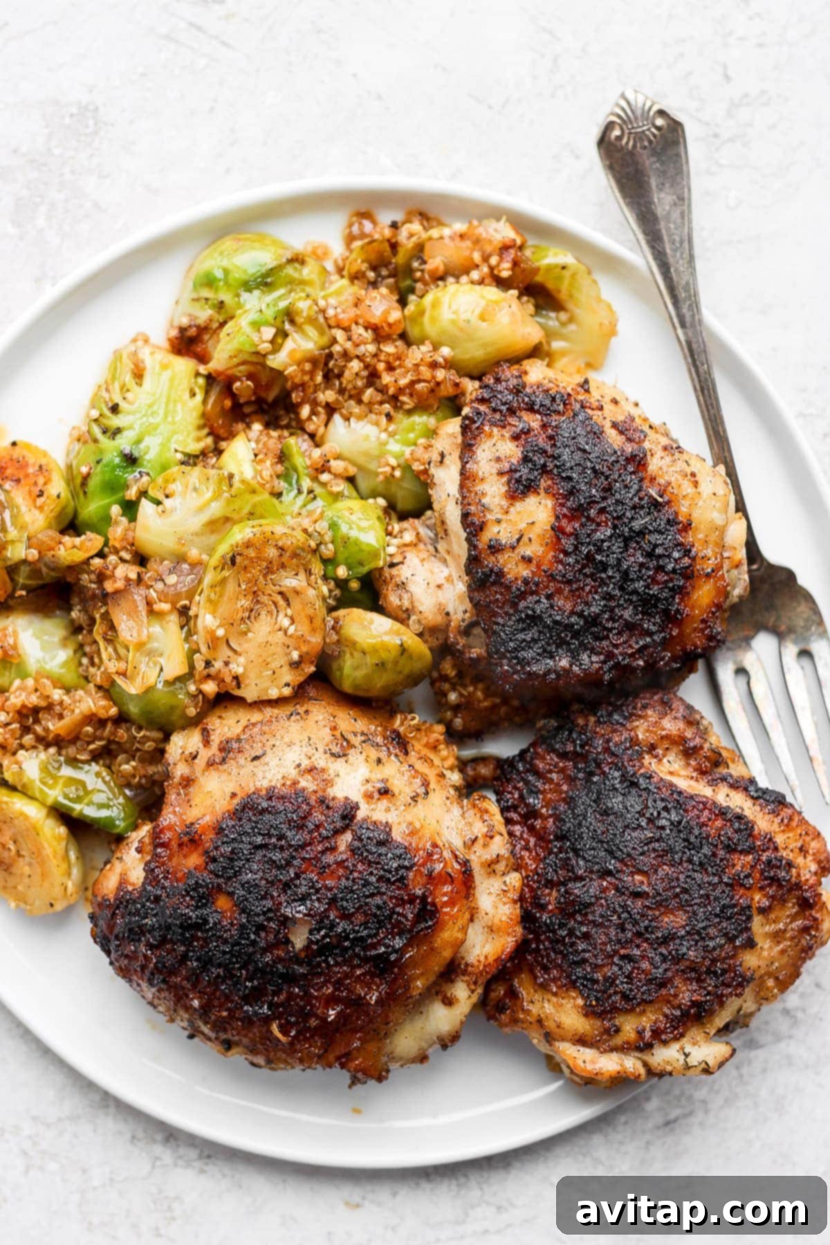 A delicious serving of Dutch oven chicken thighs with crispy skin, tender Brussels sprouts, and fluffy quinoa on a plate.