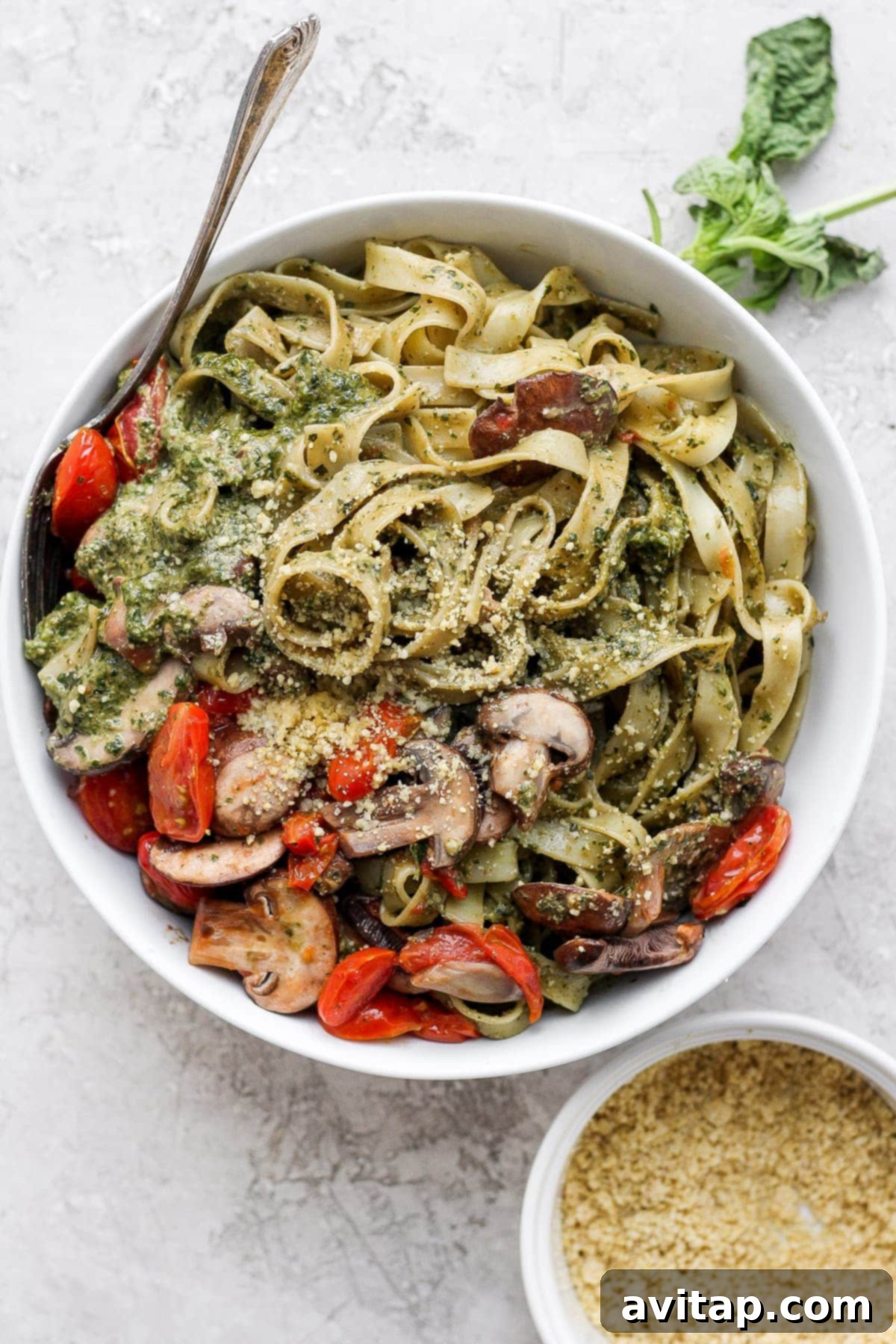 A beautifully plated bowl of pesto pasta, garnished with fresh basil leaves and a sprinkle of Parmesan cheese.