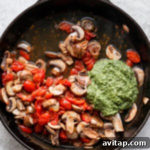 mushrooms and tomatoes in a skillet with pesto sauce.