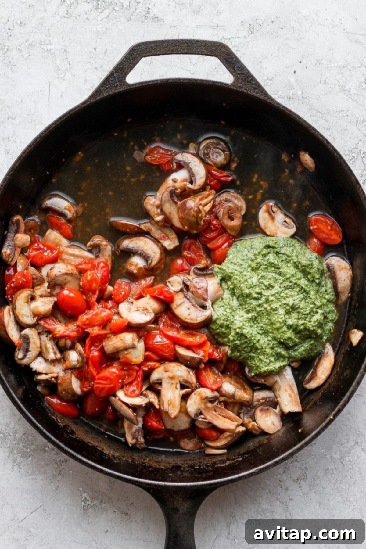Homemade pesto and sautéed cherry tomatoes and mushrooms mixed together in a cast iron skillet.