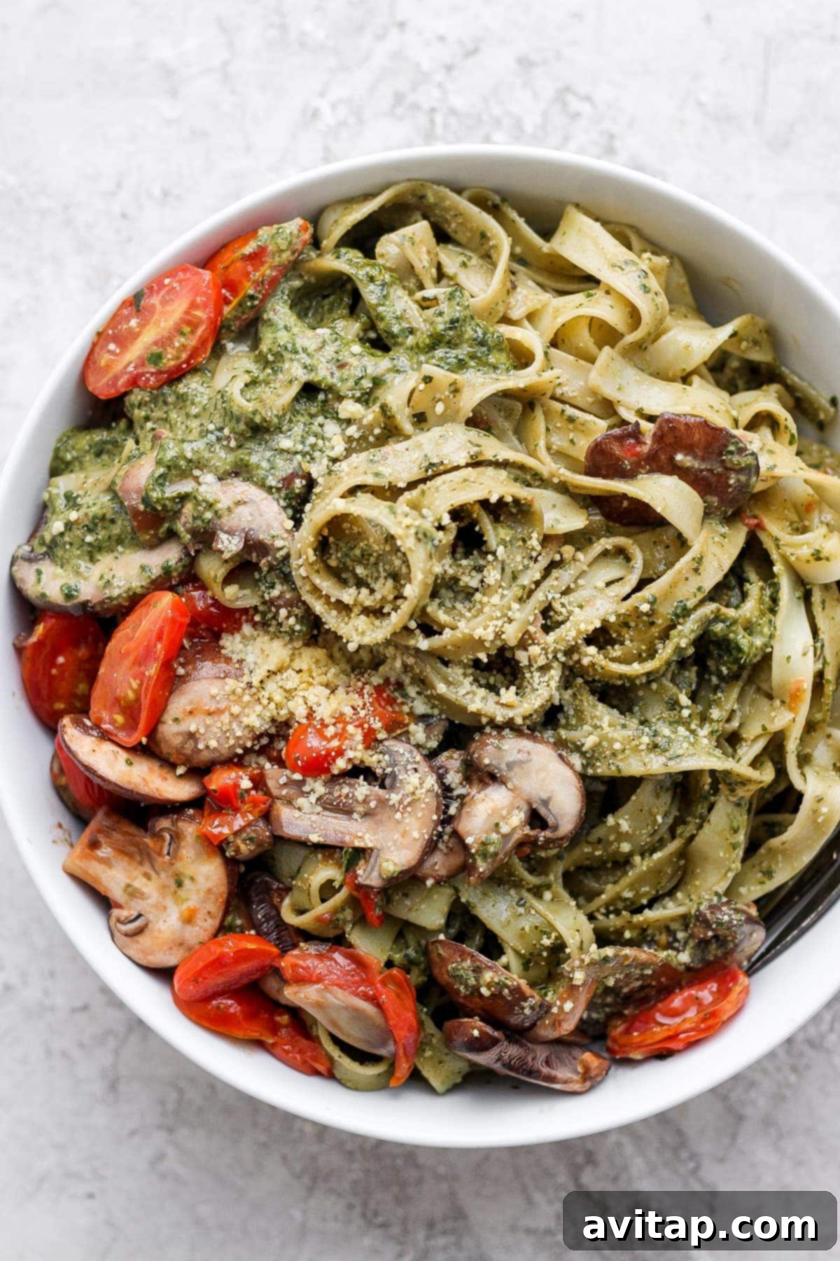 A generous serving of vegan pesto pasta, beautifully plated and garnished with fresh basil, cherry tomatoes, and a sprinkle of vegan Parmesan.