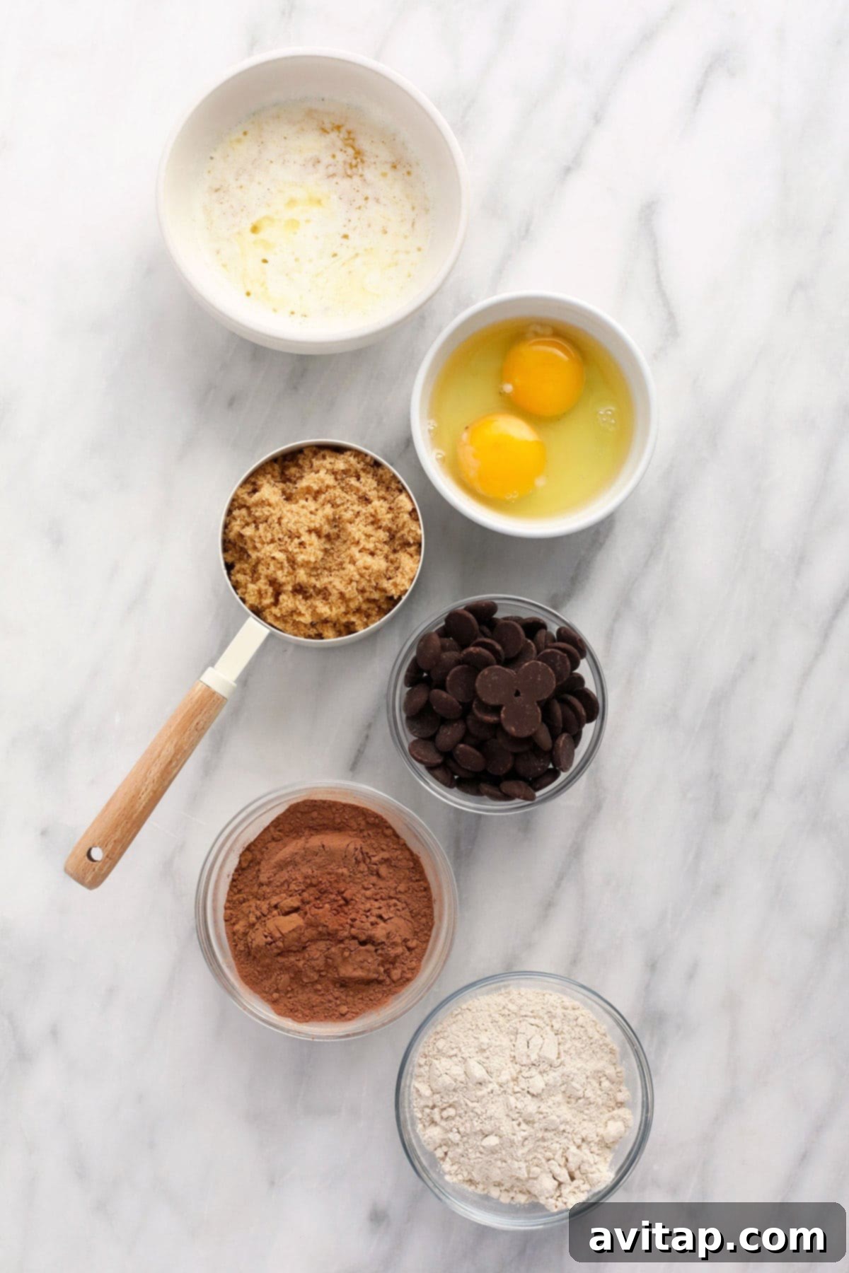Essential ingredients for homemade fudgy brownies: butter, eggs, brown sugar, chocolate chips, cocoa powder, and flour laid out.