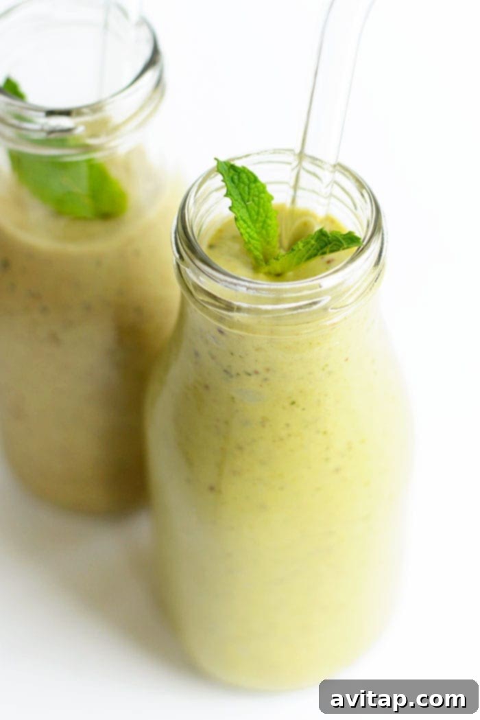 A photo of an avocado banana smoothie in two glasses with a fresh mint garnish
