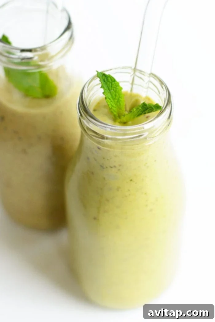 Two glasses of refreshing minty avocado banana smoothie, garnished with fresh mint leaves and chocolate chips on top.
