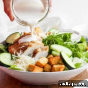 Creamy homemade Caesar dressing being poured from a small bowl over a fresh chicken Caesar salad, enhancing its flavor.