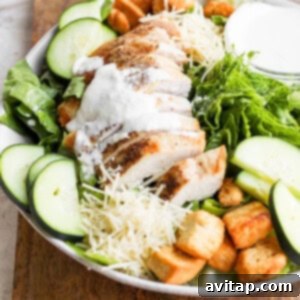 A freshly tossed chicken Caesar salad with dressing, croutons, and chicken, beautifully presented on a wooden cutting board, ready to be served.