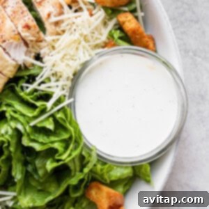 A close-up of creamy homemade Caesar dressing in a small bowl, garnished with herbs, perfect for a fresh salad.