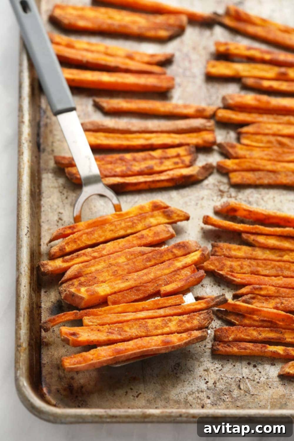 A close-up of perfectly crispy baked sweet potato fries, glistening with seasoning.