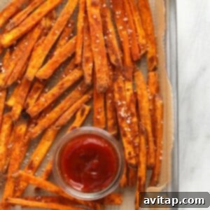 Baked sweet potato fries on a baking sheet with a side of ketchup.