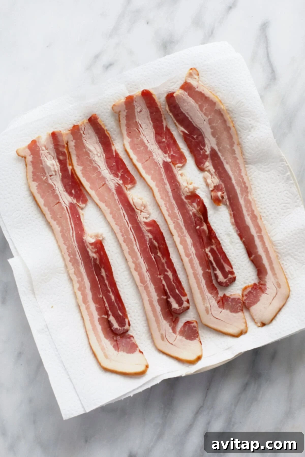 Raw bacon strips neatly arranged on a microwave-safe plate, resting on several layers of paper towel.