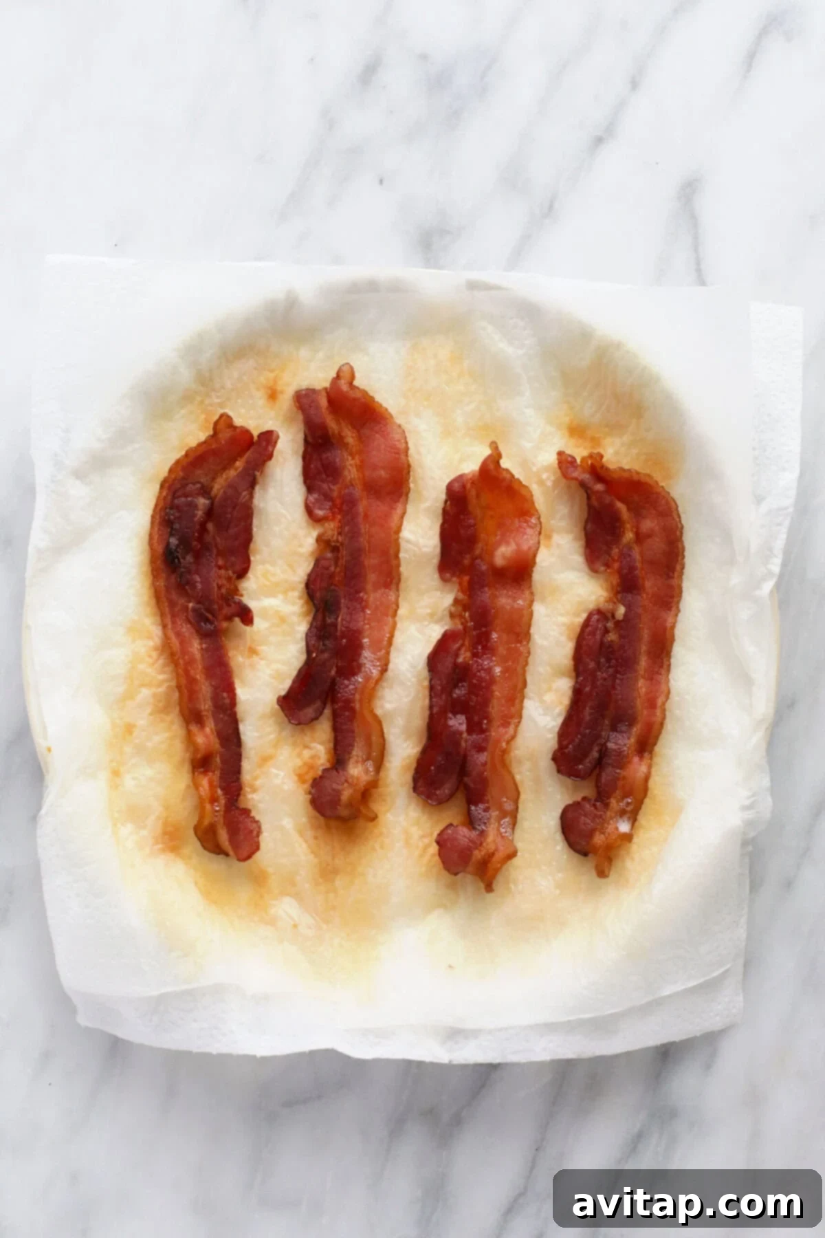 A plate covered with paper towels, displaying perfectly cooked, golden-brown bacon strips, hot and crispy from the microwave.