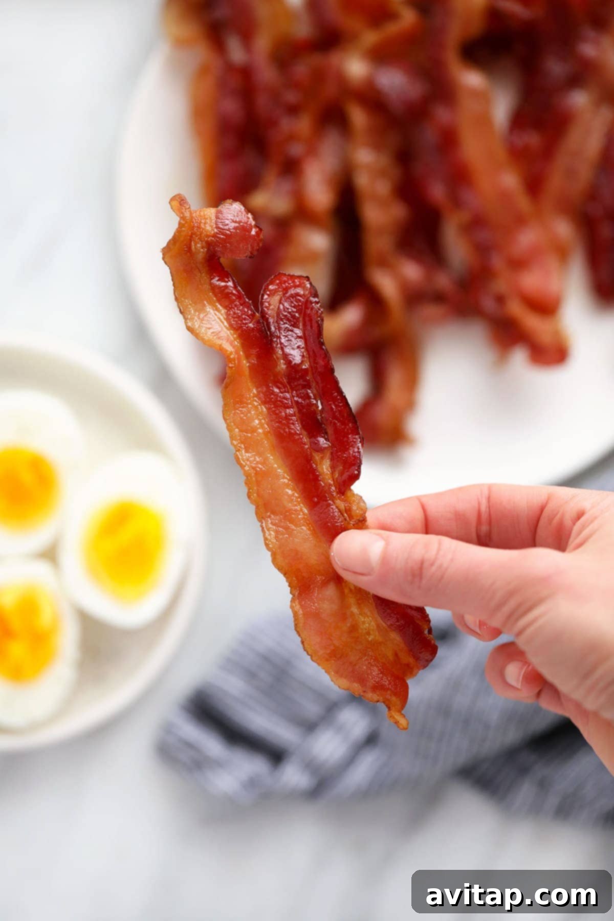 A hand holding a perfectly cooked, crispy strip of microwave bacon, ready to be enjoyed or added to a dish.
