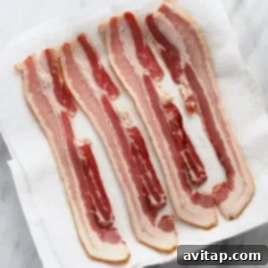 Uncooked bacon strips laid out on a paper towel-lined microwave plate.