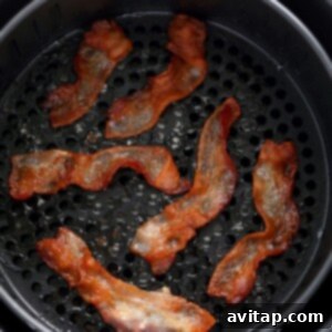 Bacon cooking inside an air fryer, with steam visible and the edges beginning to crisp and curl.