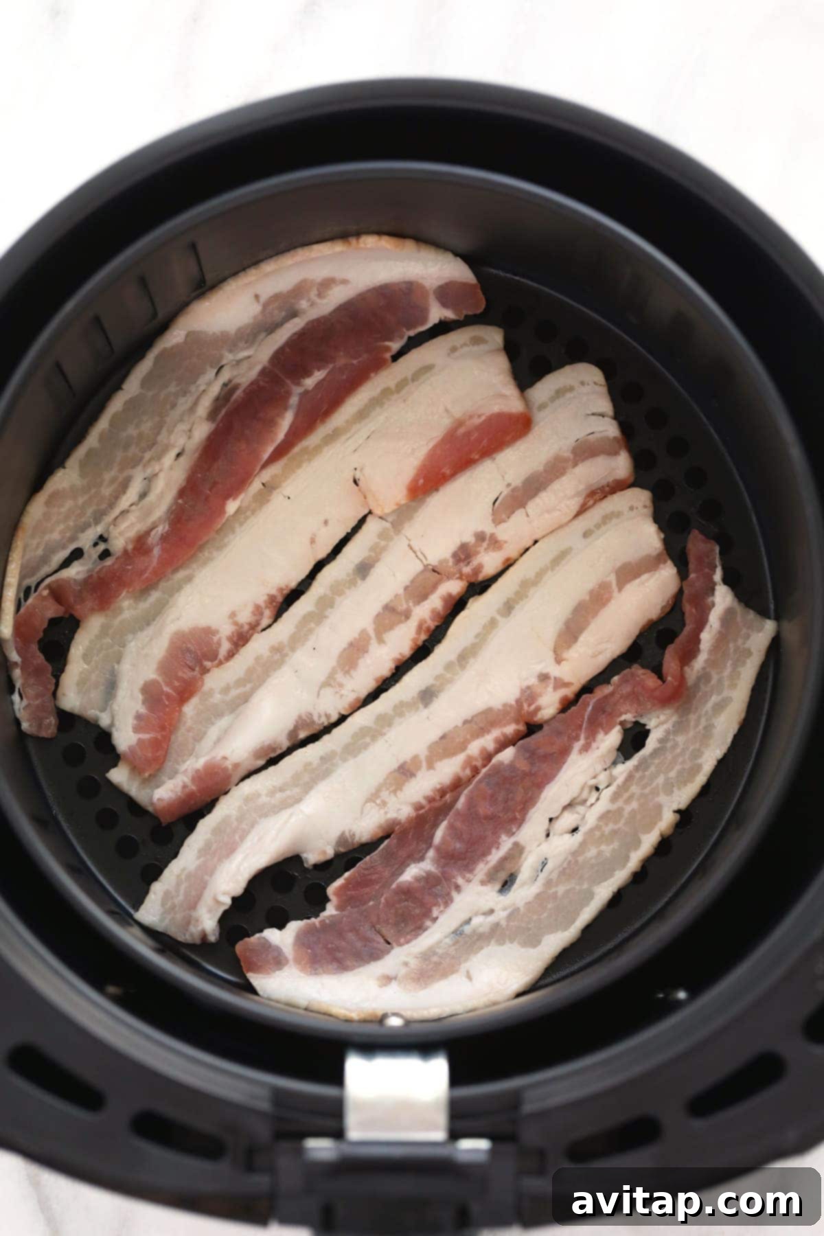 Raw bacon strips neatly arranged in a single layer inside an air fryer basket, perfectly spaced for even cooking.