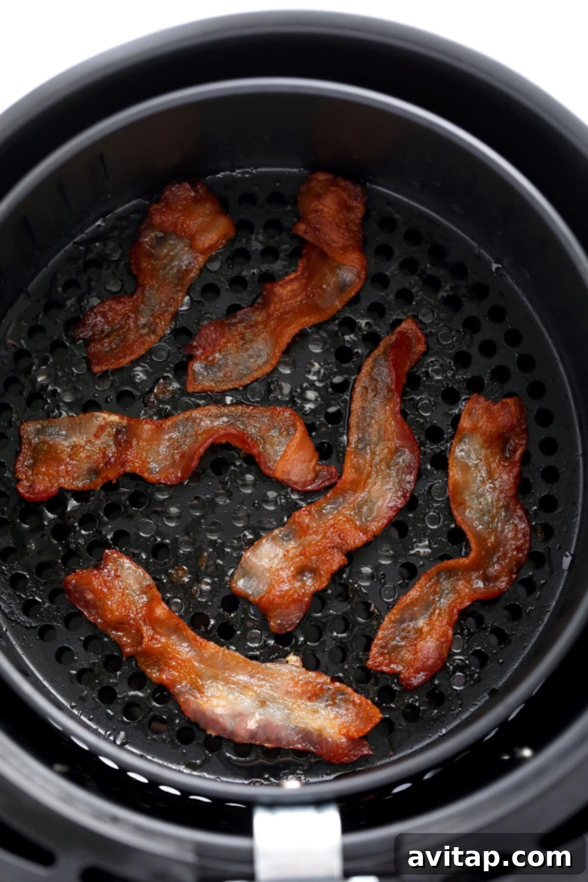 Crispy bacon sizzling enticingly in an air fryer basket, showcasing its perfectly rendered fat and golden-brown edges.