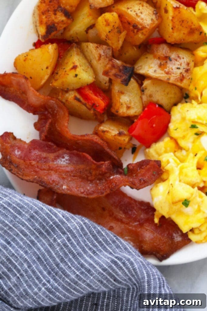 A delicious breakfast plate featuring perfectly cooked air-fried bacon, fluffy scrambled eggs, and seasoned breakfast potatoes.