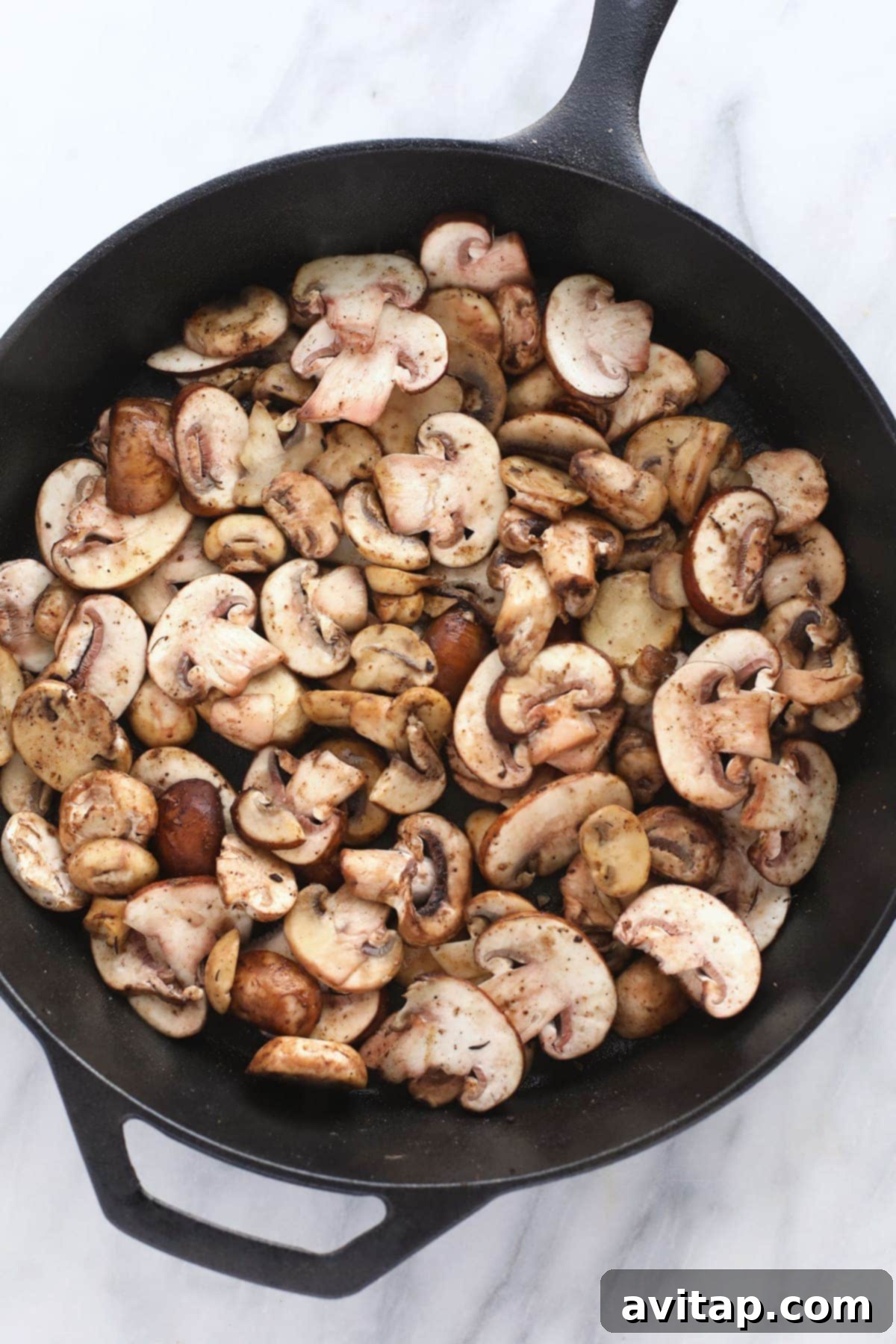Sliced crimini and bella mushrooms sautéing in a cast iron skillet, ready for the sauce