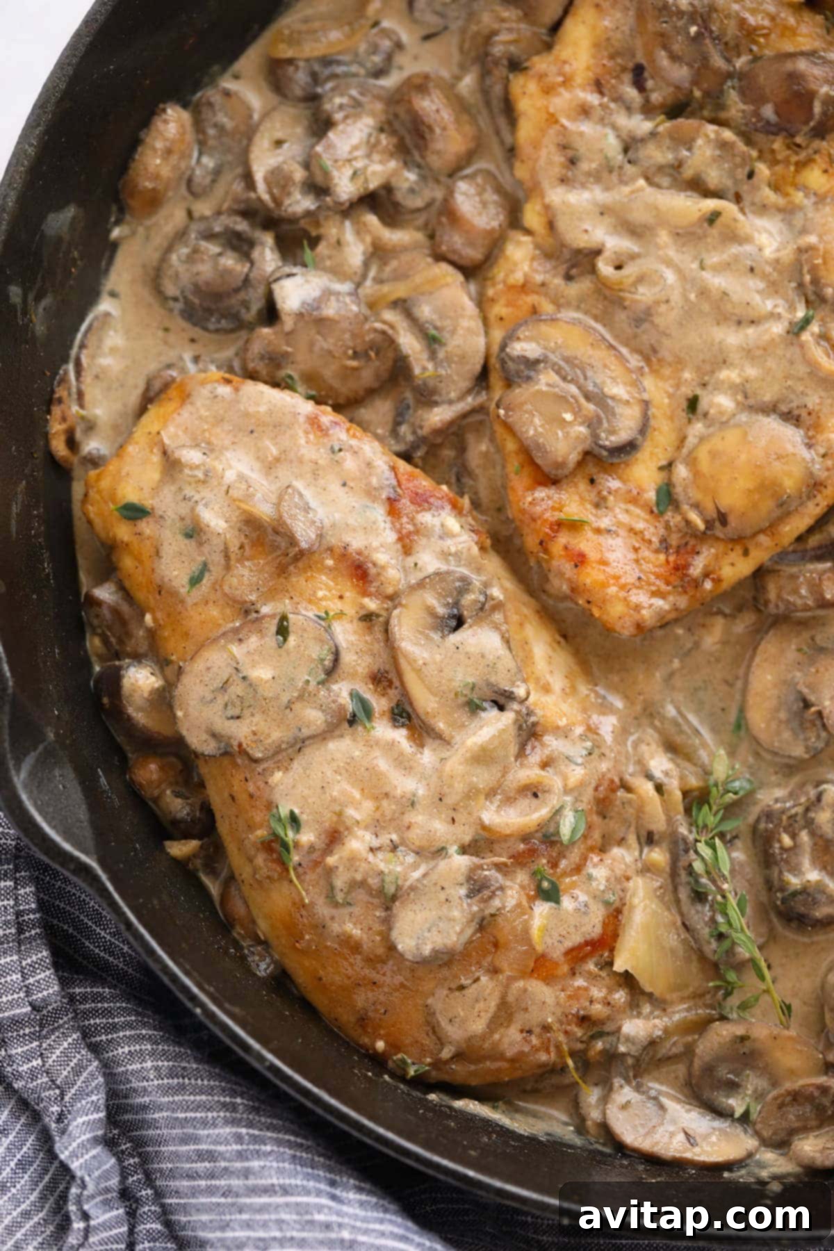 Rich Marsala mushroom sauce being poured over golden chicken breasts in a cast iron skillet