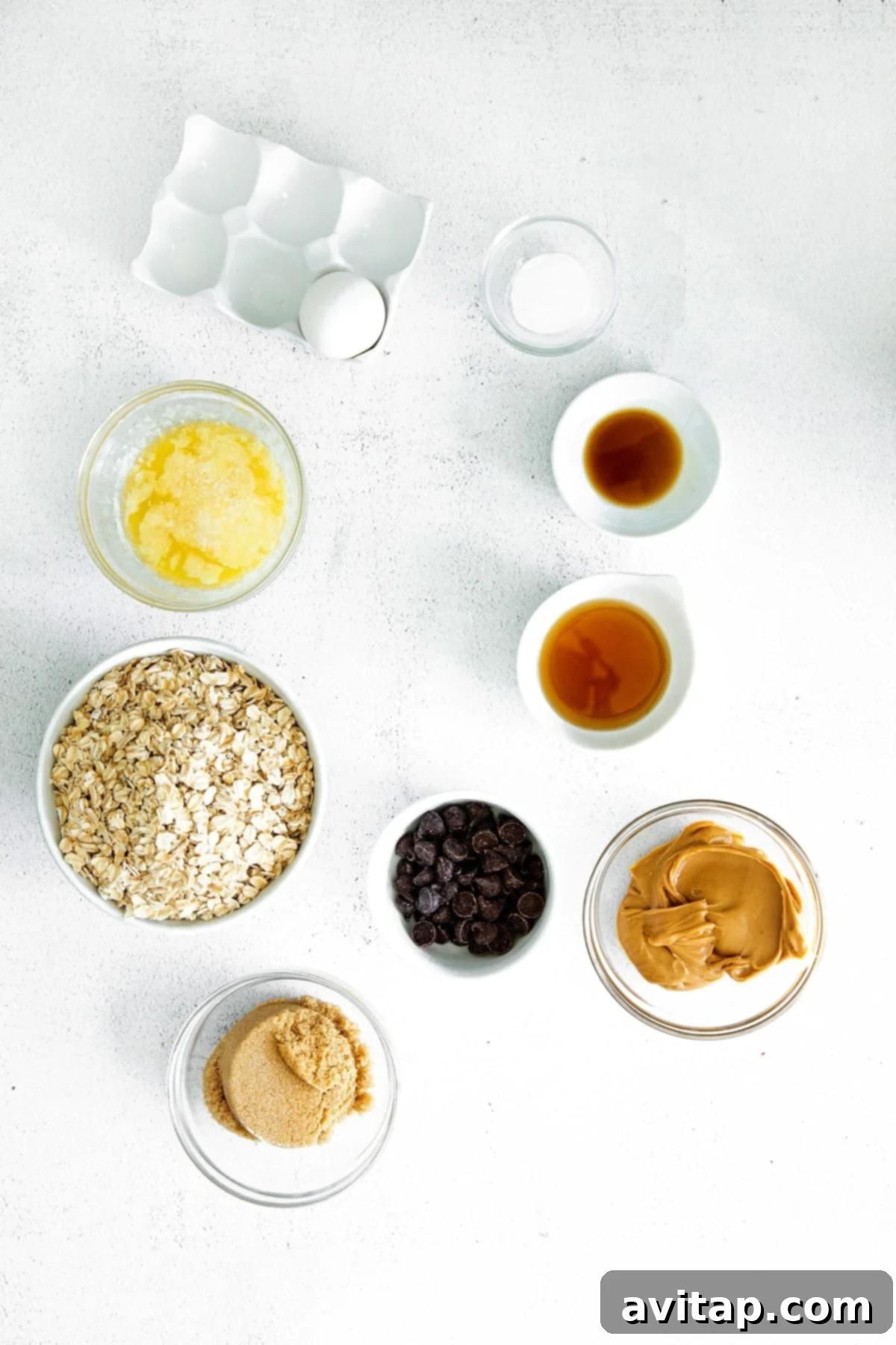 A collection of ingredients for peanut butter oatmeal cookies laid out on a surface, including oats, peanut butter, butter, brown sugar, and an egg.