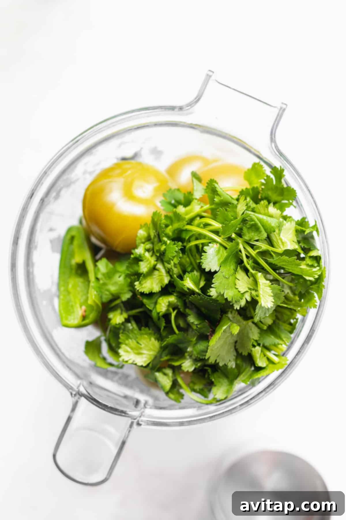 All the cooked ingredients, including tender tomatillos, onion, garlic, and peppers, gathered in a food processor, ready to be blended into a luscious salsa verde.