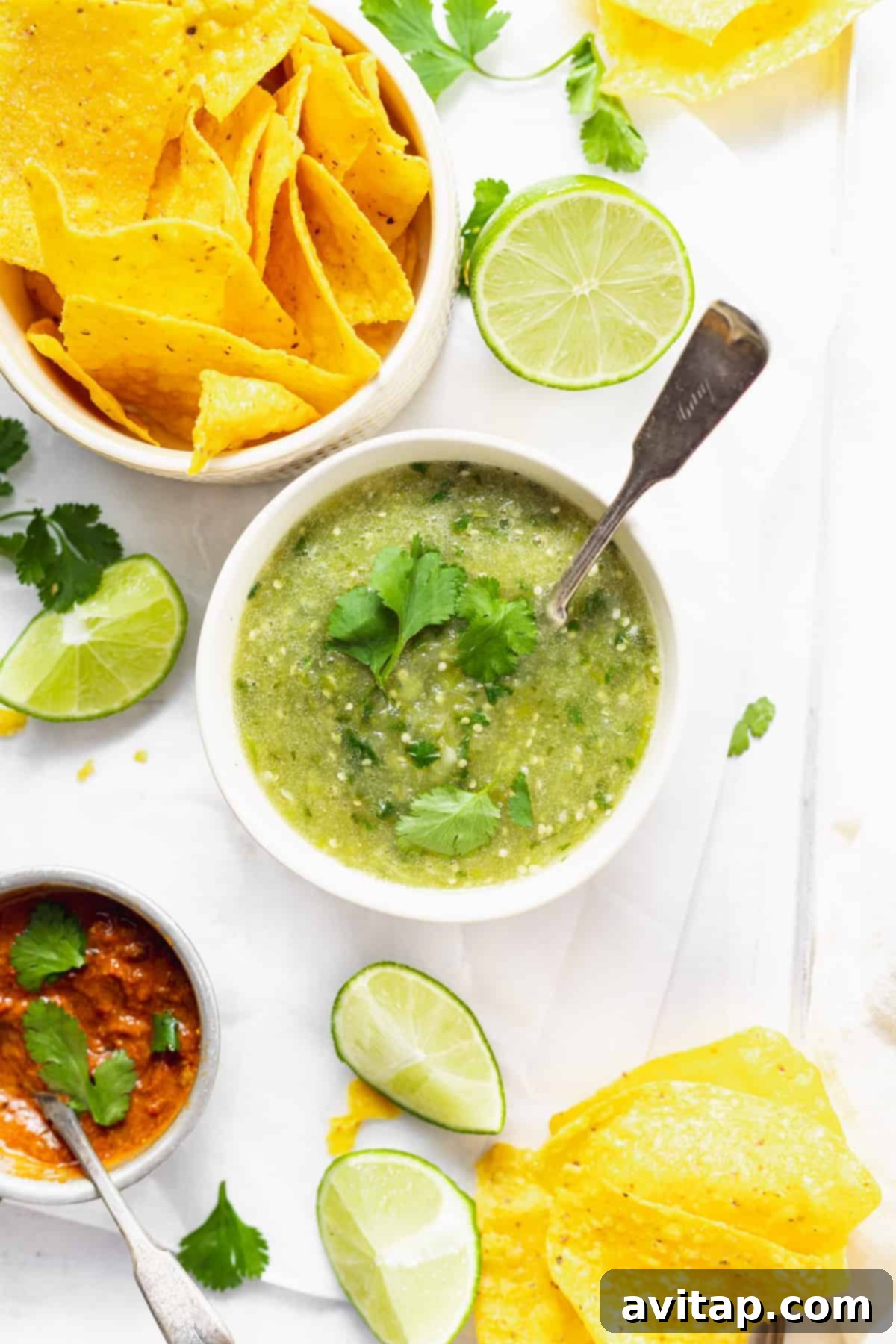 A beautifully arranged bowl of vibrant salsa verde, surrounded by golden, crispy tortilla chips and fresh lime wedges, eagerly awaiting to be enjoyed.