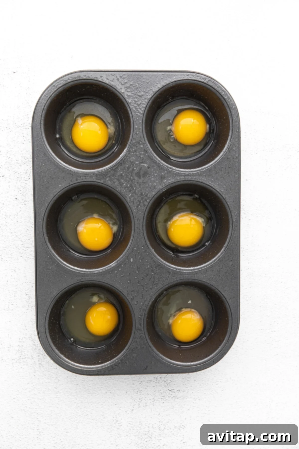 Raw eggs cracked into a greased nonstick muffin tin, ready for baking.