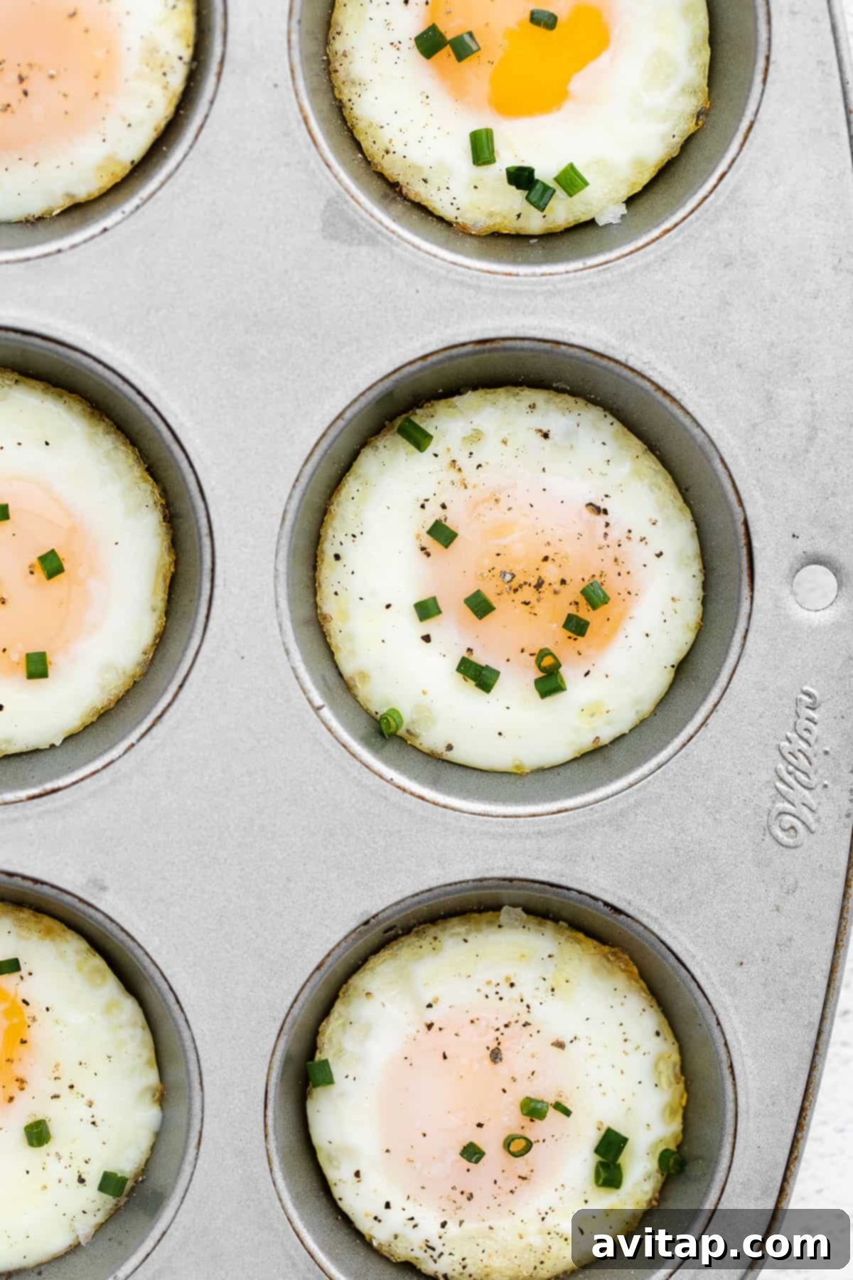 Freshly baked eggs in a muffin tin, garnished with vibrant chives.