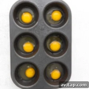 Raw eggs cracked into a muffin tin, ready for seasoning and baking.
