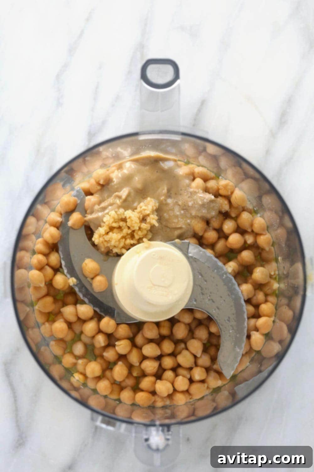 All the fresh ingredients for lemon garlic hummus, including chickpeas, olive oil, tahini, lemon, and garlic, prepared and ready in a food processor