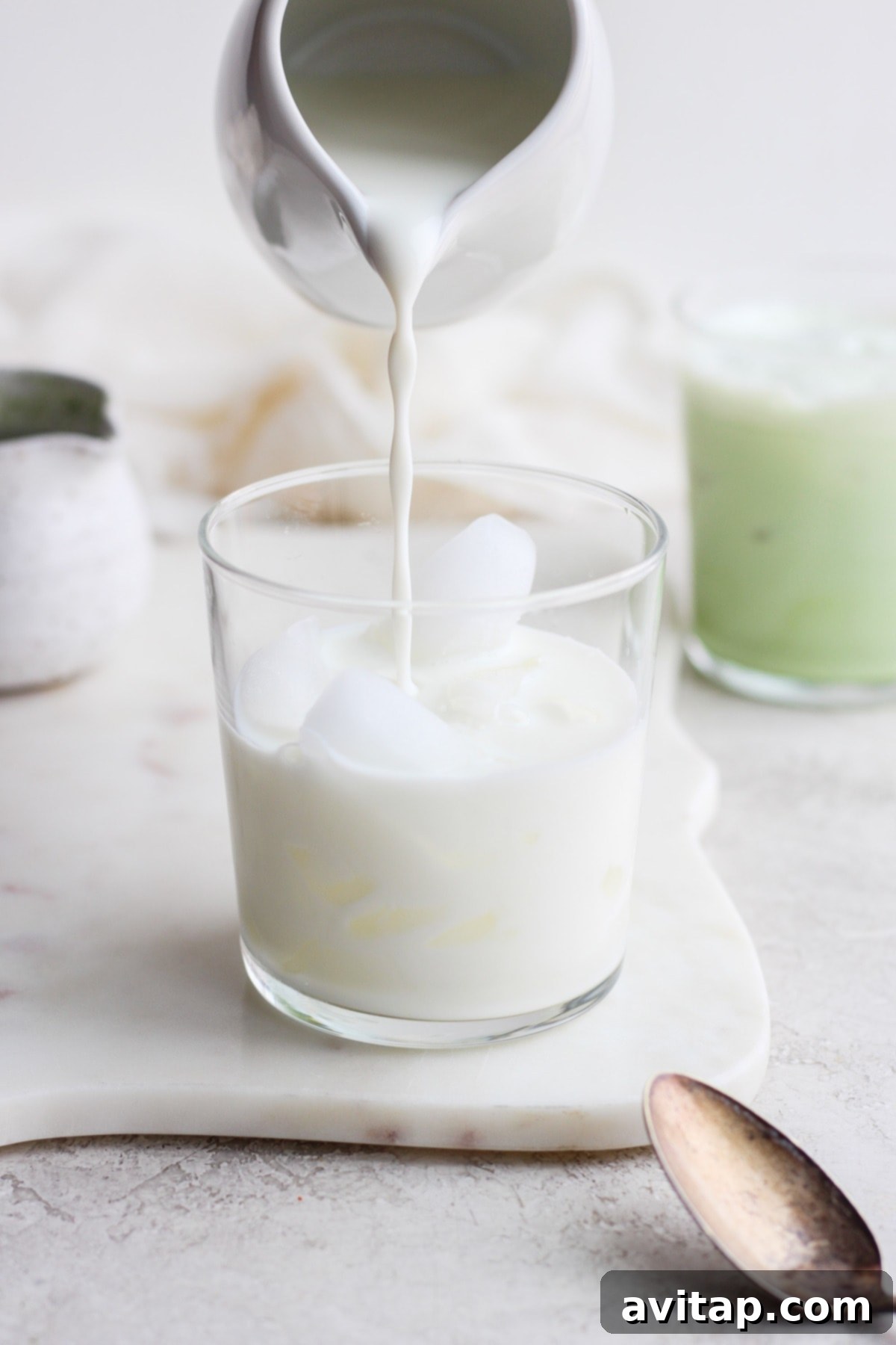 Close-up shot of almond milk and maple syrup being poured over ice in a glass, ready for the matcha mixture.