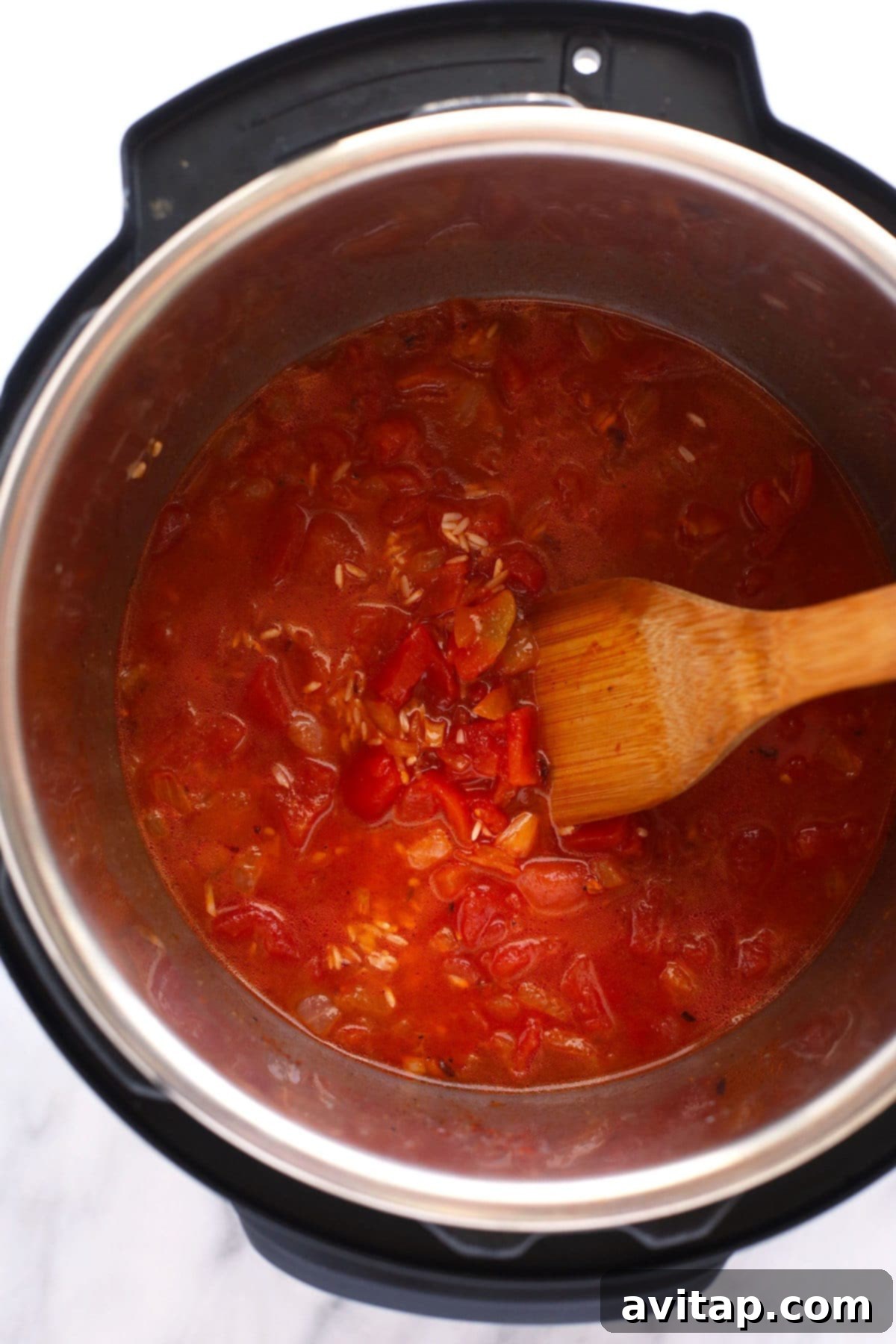 Close-up shot of the savory liquid and various ingredients simmering inside an Instant Pot, showing the cooking process of jambalaya.