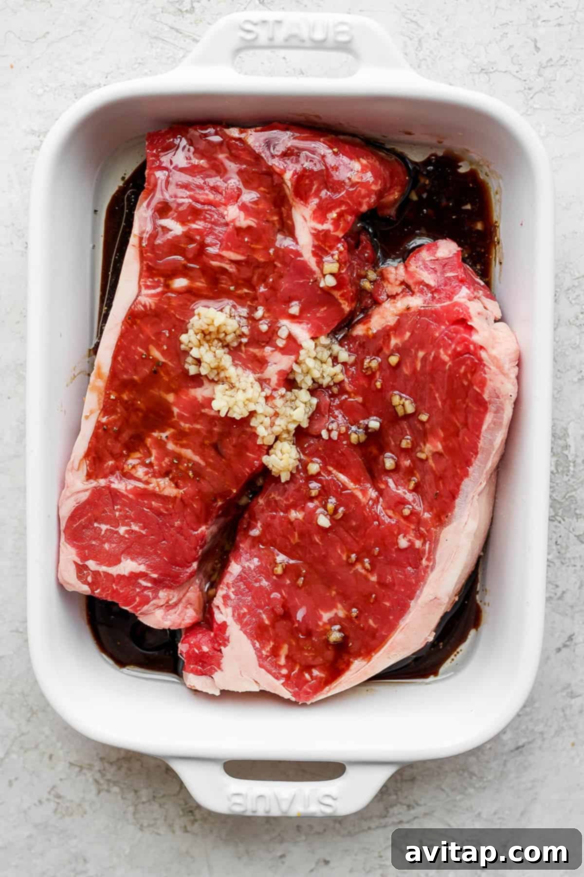 Raw steaks marinating in a clear baking dish, soaking up the flavorful liquid.