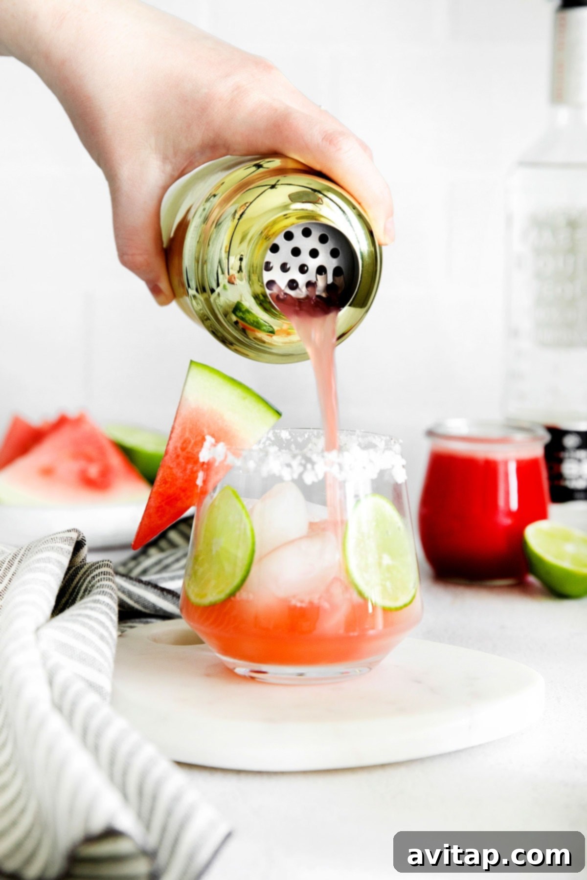 A close-up of a refreshing watermelon margarita being poured over ice into a glass, highlighting its vibrant color and frosty appeal.