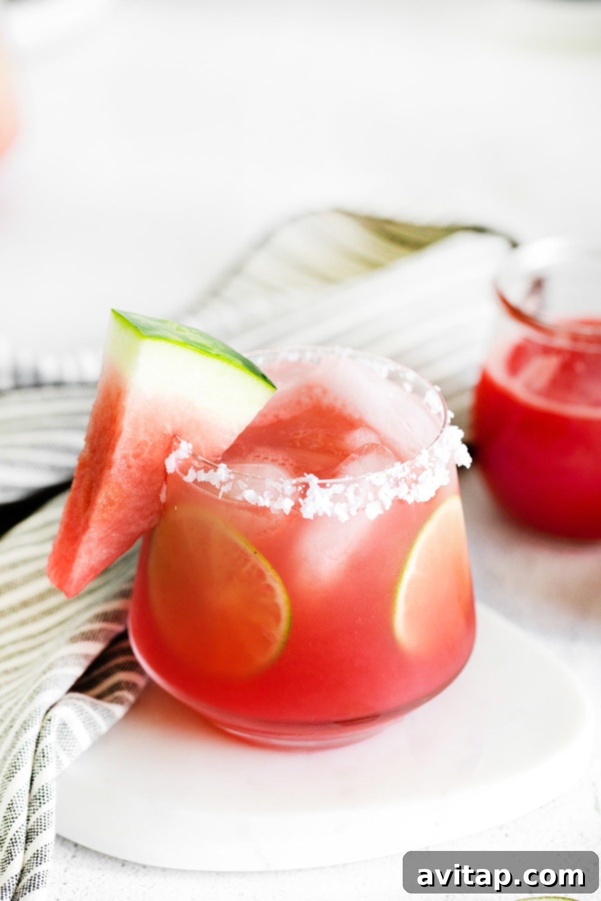 A beautifully presented watermelon margarita in a glass with a perfectly salted rim, garnished with vibrant lime rounds and fresh watermelon slices, ready to be enjoyed.
