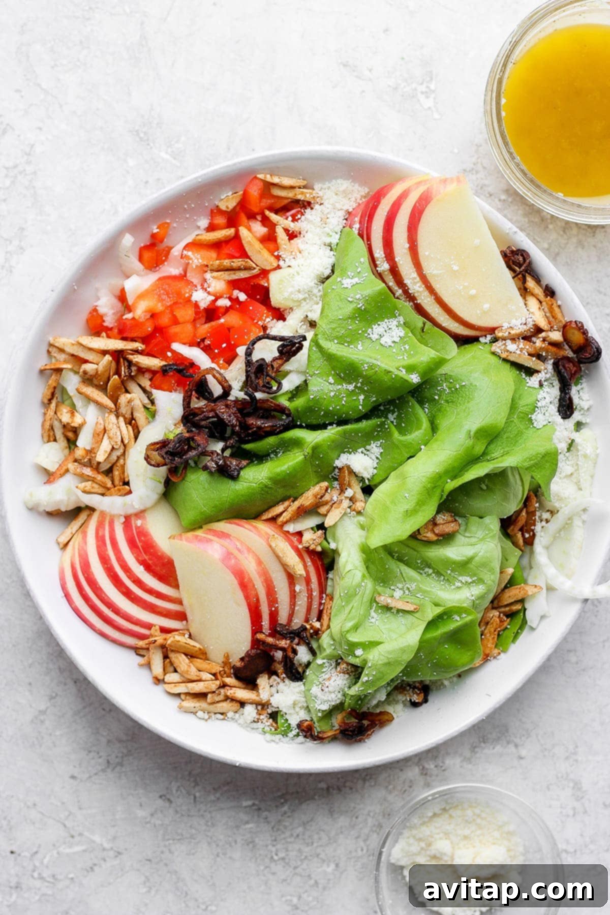 A vibrant butter lettuce salad brimming with crisp apples, colorful bell peppers, golden slivered almonds, and grated Parmesan cheese, served in a large salad bowl.