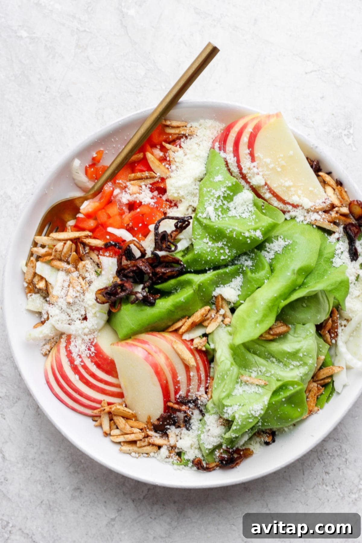 A beautifully presented butter lettuce salad in a large bowl, showcasing its fresh vegetables, fruit, cheese, and lemon vinaigrette, ready to be enjoyed.