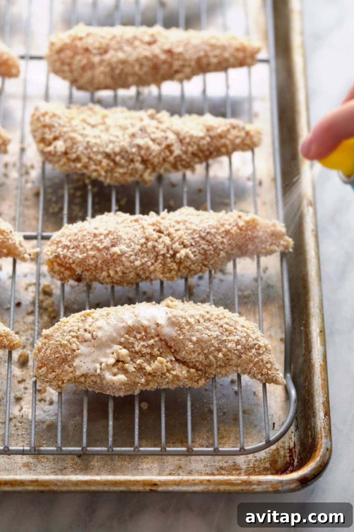 Golden Baked Chicken Fingers 6 Crispy baked chicken tenders arranged on a metal baking rack over a sheet pan.