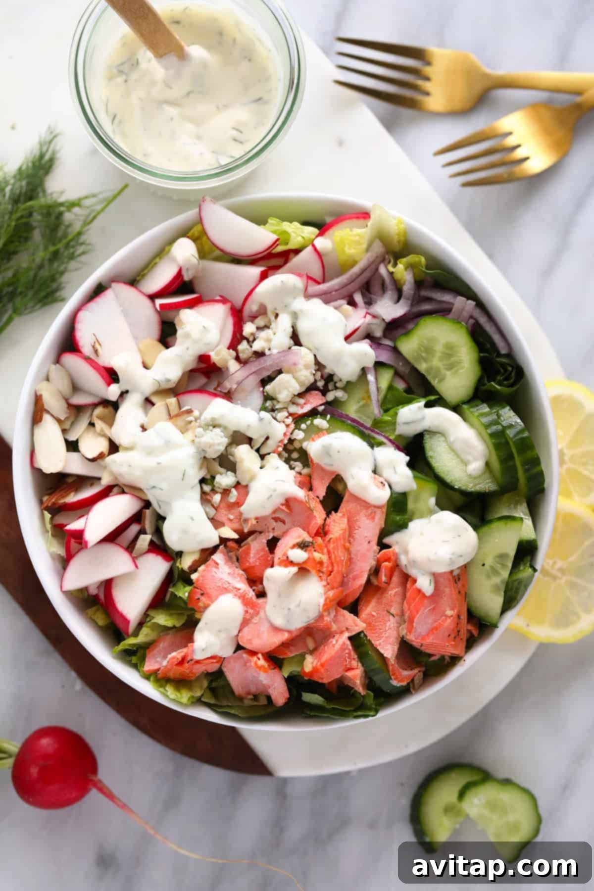 A beautifully presented salmon salad in a large white bowl, garnished with fresh dill and a generous drizzle of creamy Greek yogurt dressing.