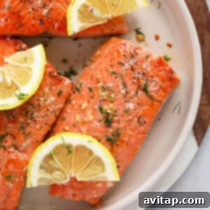 Golden-brown pan-seared salmon on a white plate, garnished with lemon wedges and fresh dill.