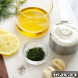 The fresh ingredients for a dill dressing laid out on a cutting board, including fresh dill, lemon, garlic, and plain Greek yogurt.