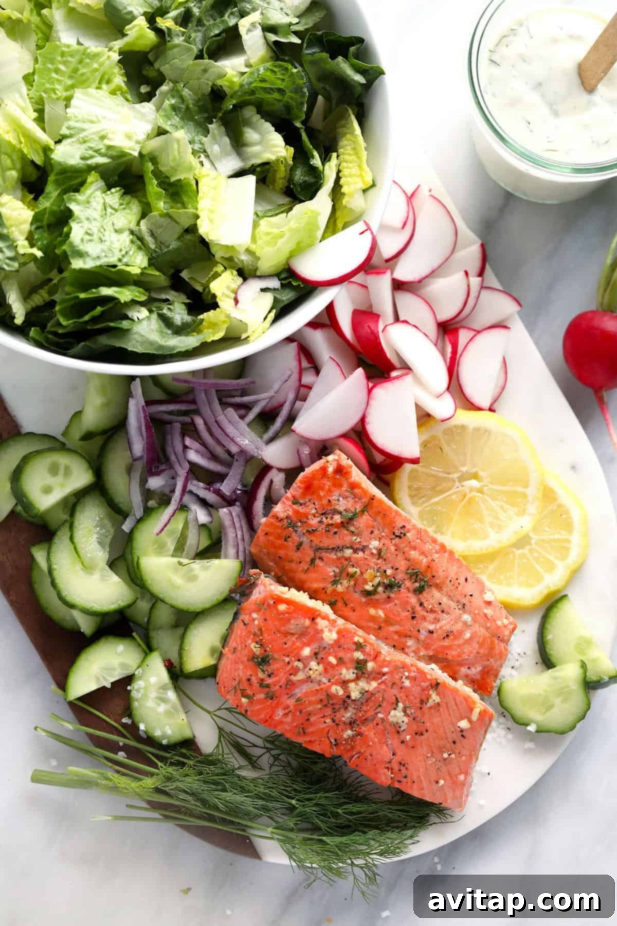 An inviting assortment of fresh salad vegetables, a vibrant lemon, and perfectly cooked salmon fillets are artfully arranged on a rustic cutting board, signaling readiness for salad assembly.